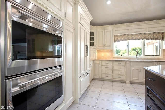 kitchen with decorative backsplash, light tile patterned floors, sink, and double oven