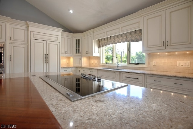 kitchen featuring black electric stovetop, tasteful backsplash, light stone counters, vaulted ceiling, and sink