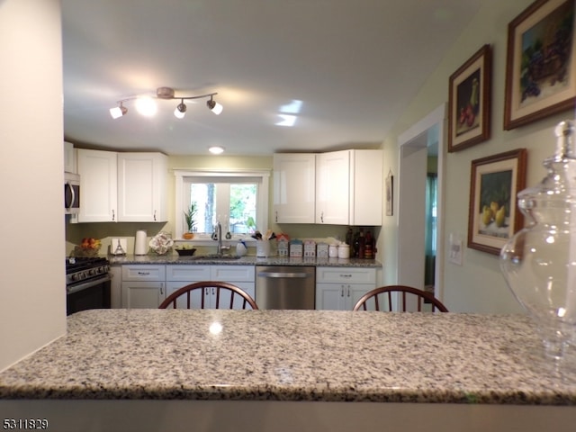 kitchen with light stone counters, white cabinets, sink, kitchen peninsula, and stainless steel appliances