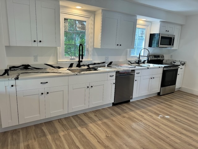 kitchen with white cabinets, stainless steel appliances, sink, and light wood-type flooring