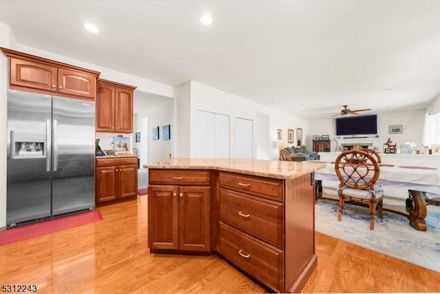 kitchen featuring light hardwood / wood-style floors, light stone counters, ceiling fan, a kitchen island, and stainless steel fridge with ice dispenser