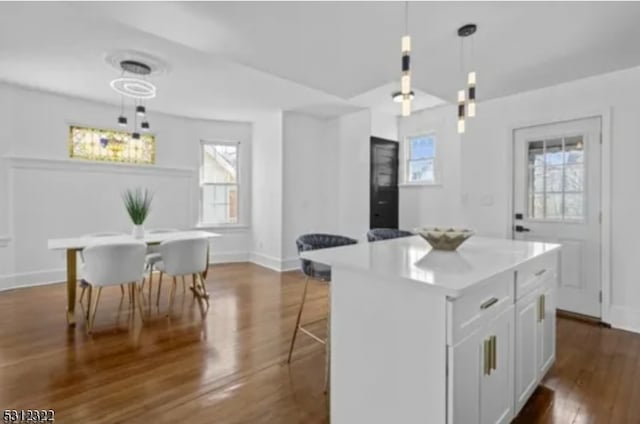 kitchen with a kitchen island, decorative light fixtures, a breakfast bar, dark wood-type flooring, and white cabinetry