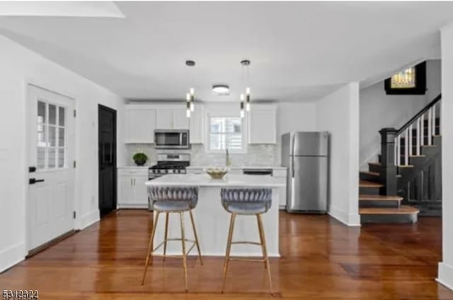 kitchen with a kitchen bar, dark hardwood / wood-style flooring, stainless steel appliances, and white cabinetry