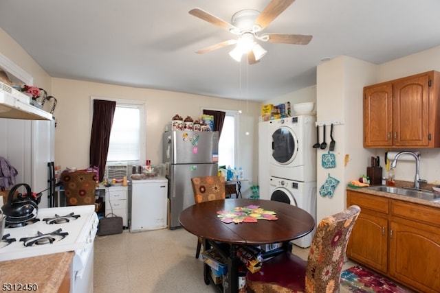 kitchen with ceiling fan, sink, stacked washer and dryer, and white appliances