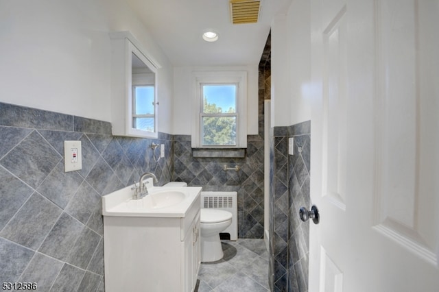 bathroom with vanity, radiator heating unit, a shower, tile walls, and toilet