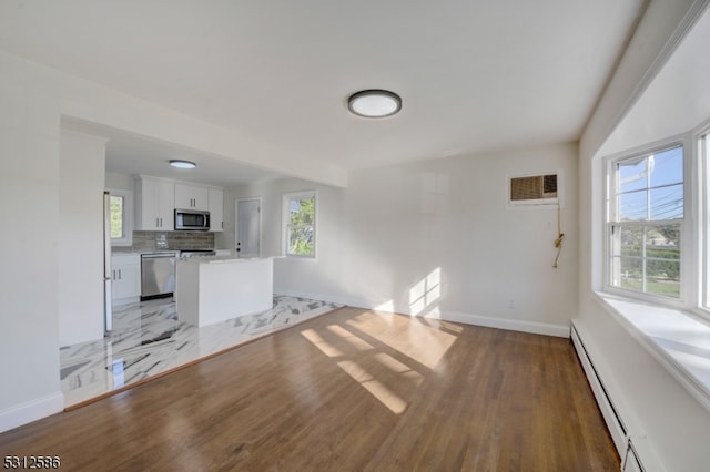 unfurnished living room featuring hardwood / wood-style flooring, a wealth of natural light, and a baseboard heating unit