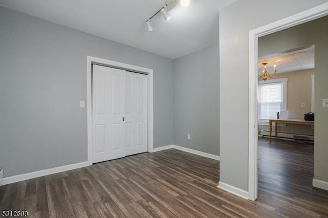 unfurnished bedroom featuring rail lighting, a baseboard radiator, dark hardwood / wood-style flooring, a notable chandelier, and a closet