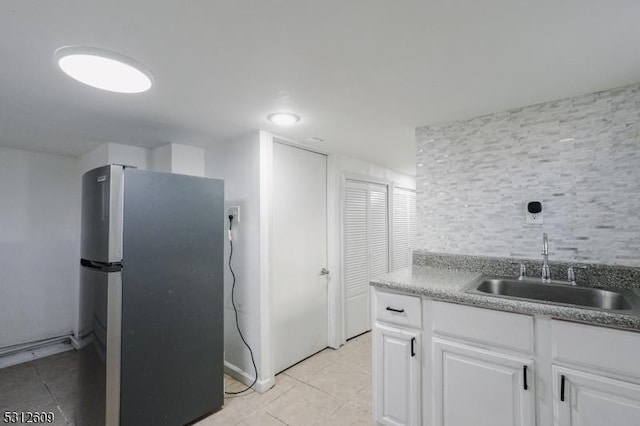 kitchen featuring stainless steel refrigerator, light tile patterned floors, sink, and white cabinets