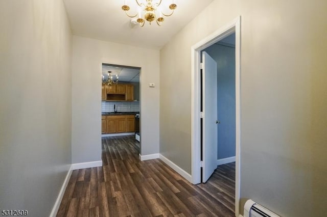 hall with an inviting chandelier, dark wood-type flooring, and a baseboard heating unit