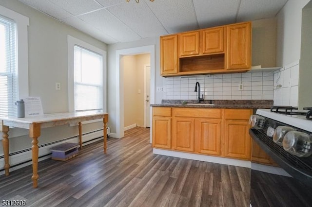 kitchen with tasteful backsplash, a baseboard radiator, sink, gas stove, and dark wood-type flooring