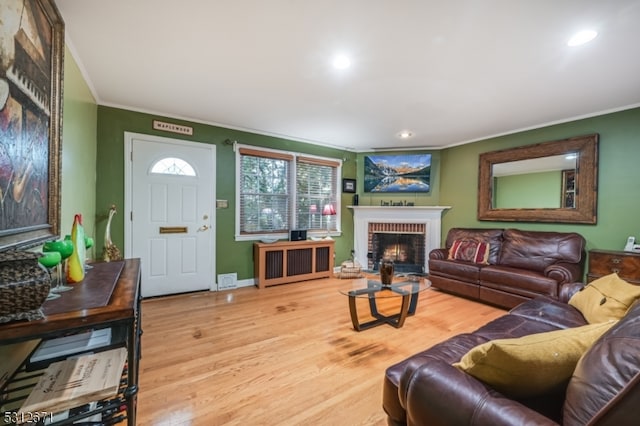 living room featuring wood-type flooring, ornamental molding, and a brick fireplace