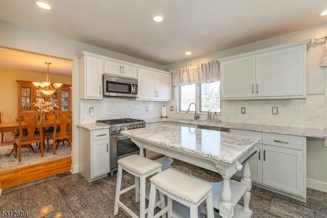 kitchen featuring appliances with stainless steel finishes, backsplash, light stone counters, pendant lighting, and white cabinets