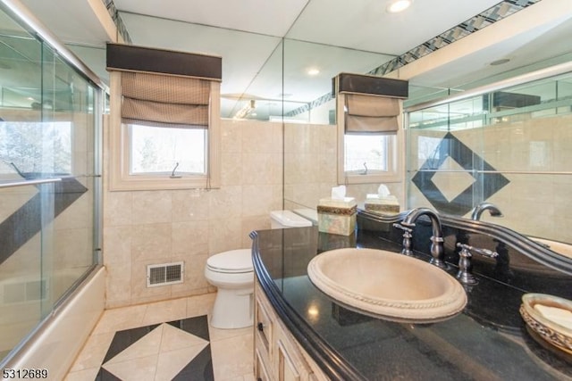 full bathroom featuring tile walls, vanity, toilet, tile patterned floors, and shower / bath combination with glass door