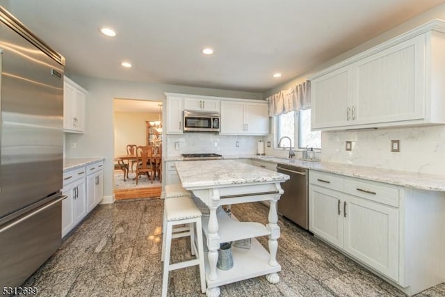 kitchen with white cabinetry, stainless steel appliances, light stone countertops, and decorative backsplash