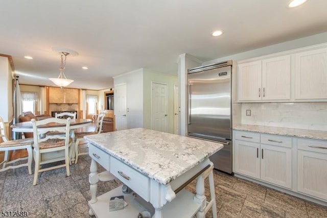 kitchen with hanging light fixtures, backsplash, light stone counters, and built in refrigerator