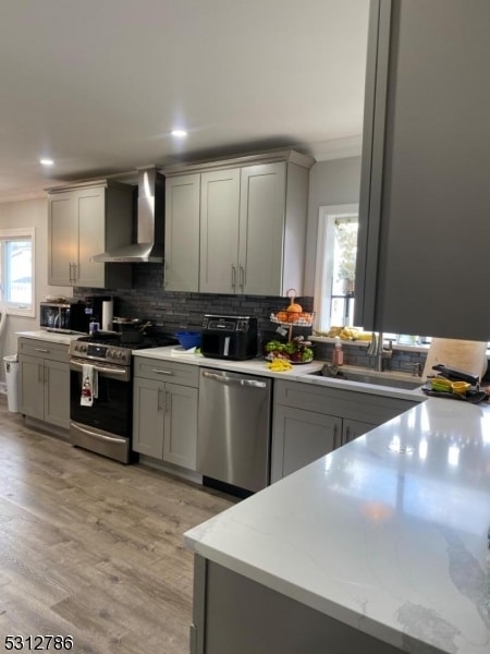 kitchen with gray cabinetry, appliances with stainless steel finishes, and wall chimney range hood