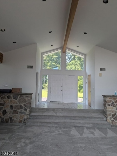 carpeted entryway with high vaulted ceiling and beamed ceiling