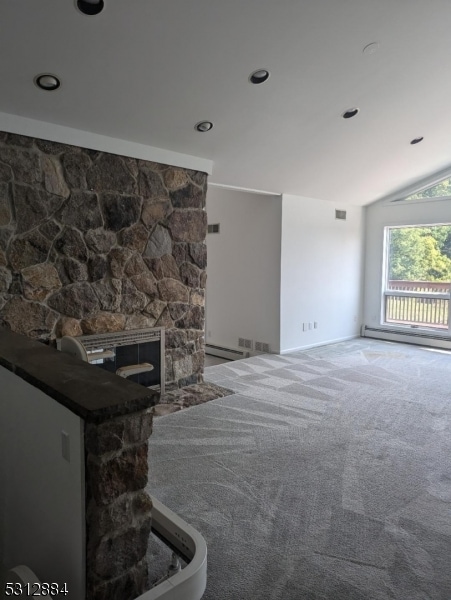 unfurnished living room featuring a stone fireplace, carpet floors, and vaulted ceiling