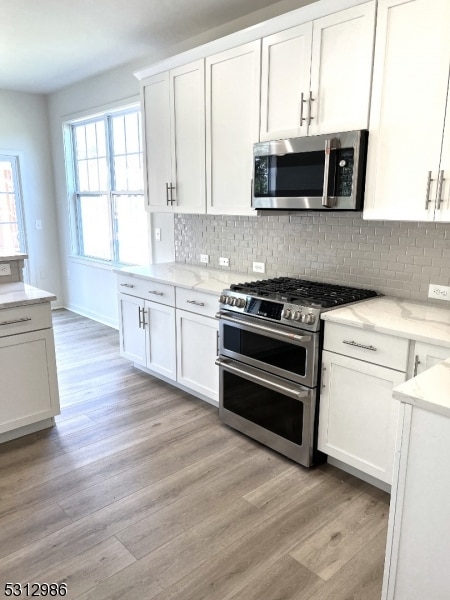 kitchen featuring white cabinetry, light hardwood / wood-style flooring, stainless steel appliances, and tasteful backsplash