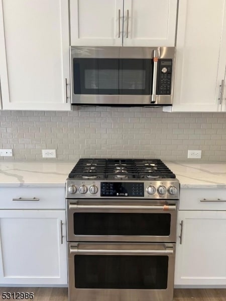 kitchen with light hardwood / wood-style flooring, backsplash, white cabinetry, appliances with stainless steel finishes, and light stone countertops