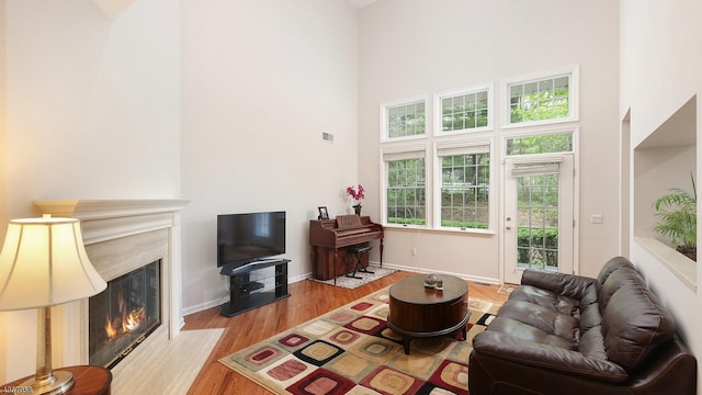 living room featuring a premium fireplace, light wood-type flooring, and a towering ceiling