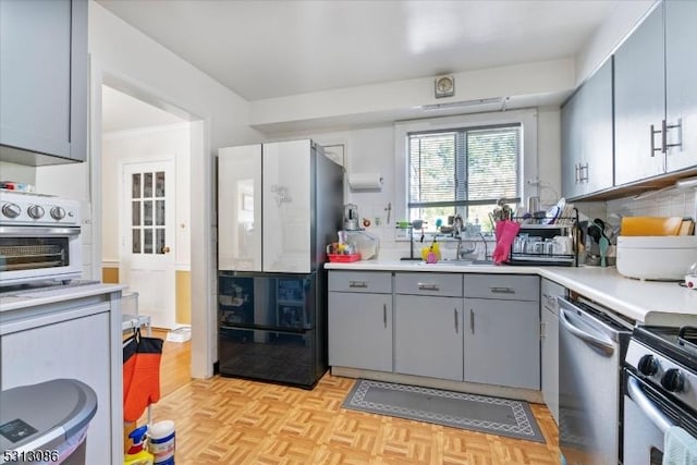 kitchen with stainless steel appliances, gray cabinetry, light parquet floors, and backsplash