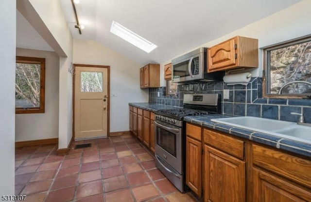 kitchen with appliances with stainless steel finishes, tasteful backsplash, vaulted ceiling, sink, and dark tile patterned flooring