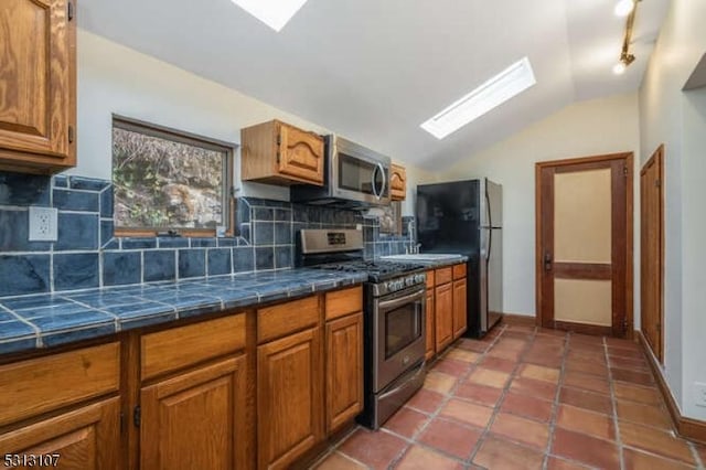 kitchen featuring tile counters, tasteful backsplash, tile patterned floors, lofted ceiling, and appliances with stainless steel finishes