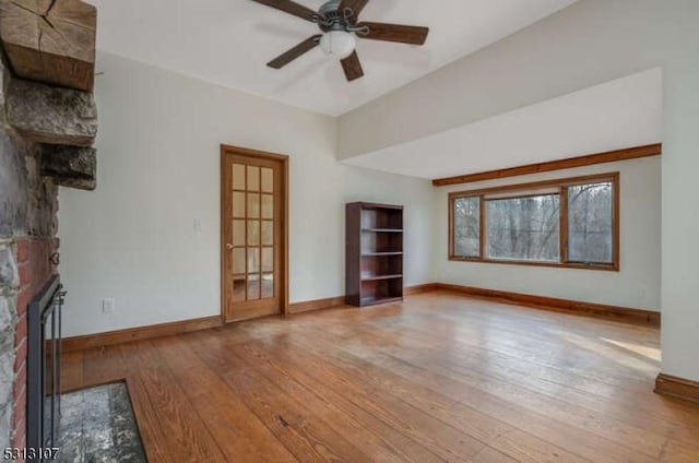 unfurnished living room with wood-type flooring, a stone fireplace, and ceiling fan