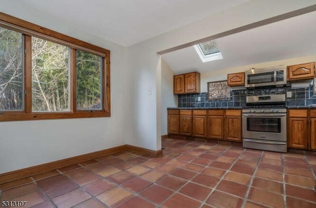 kitchen featuring dark tile patterned flooring, lofted ceiling with skylight, appliances with stainless steel finishes, and tasteful backsplash