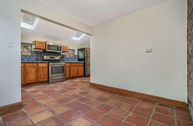 kitchen featuring vaulted ceiling with skylight, backsplash, stainless steel appliances, and tile patterned flooring