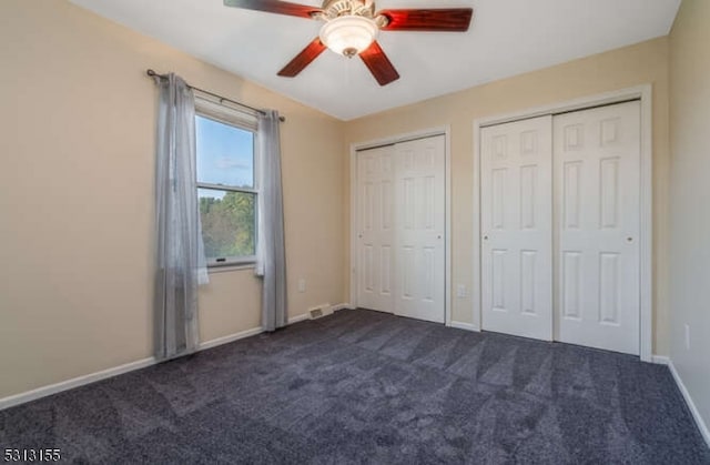 unfurnished bedroom featuring dark colored carpet, multiple closets, and ceiling fan