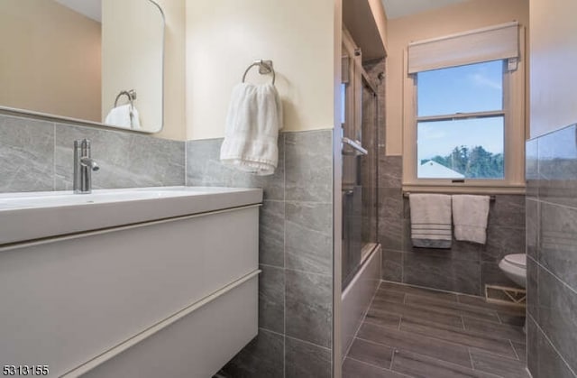 full bathroom with tile walls, enclosed tub / shower combo, vanity, and toilet