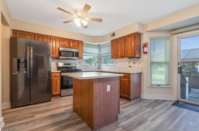 kitchen featuring ceiling fan, a kitchen island, appliances with stainless steel finishes, light hardwood / wood-style floors, and decorative backsplash