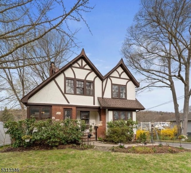english style home featuring brick siding, a front yard, stucco siding, and a chimney