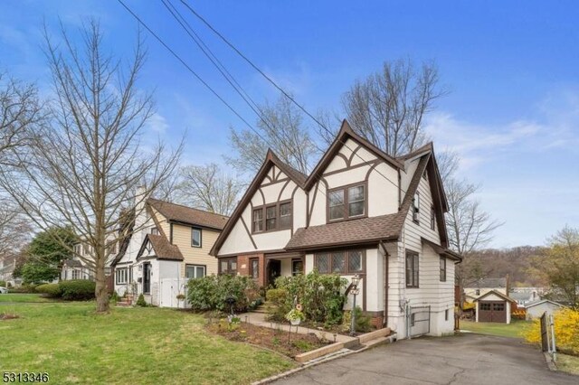 view of front of home featuring an outdoor structure, a storage unit, a shingled roof, stucco siding, and a front lawn