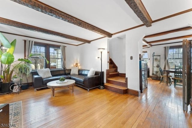 living room featuring hardwood / wood-style flooring, beamed ceiling, baseboards, ornamental molding, and stairs