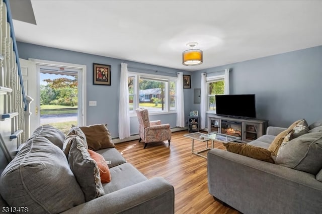 living room featuring a baseboard radiator, light hardwood / wood-style flooring, a fireplace, and a wealth of natural light