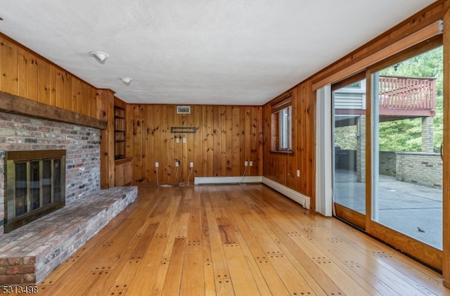 unfurnished living room with a brick fireplace, wooden walls, light hardwood / wood-style flooring, and a textured ceiling