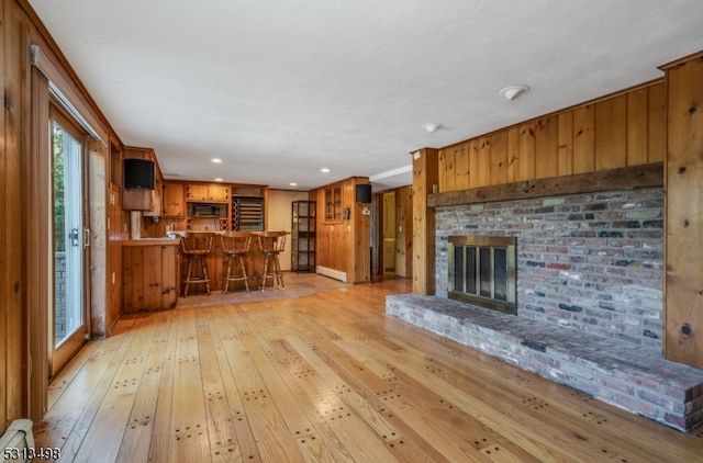 unfurnished living room with wooden walls, light hardwood / wood-style flooring, a fireplace, and indoor bar