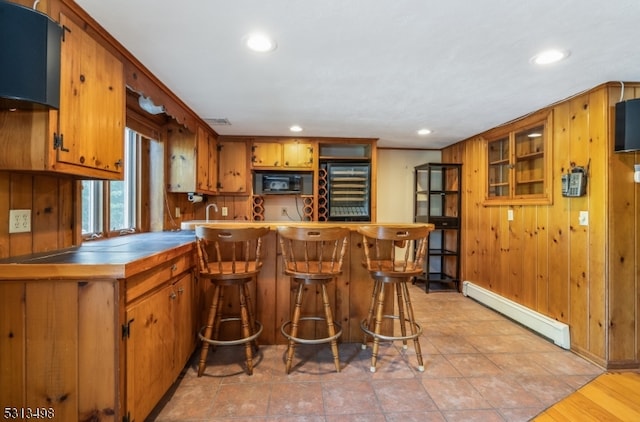 kitchen with a breakfast bar, a baseboard heating unit, kitchen peninsula, wooden walls, and black appliances