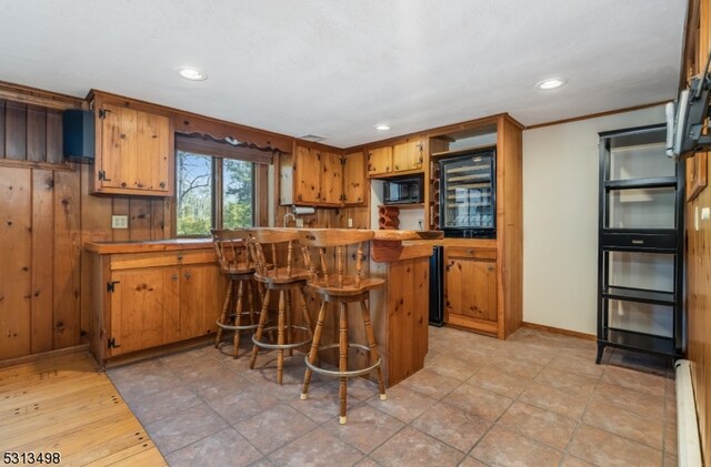 kitchen with kitchen peninsula, a kitchen bar, baseboard heating, light tile patterned floors, and ornamental molding