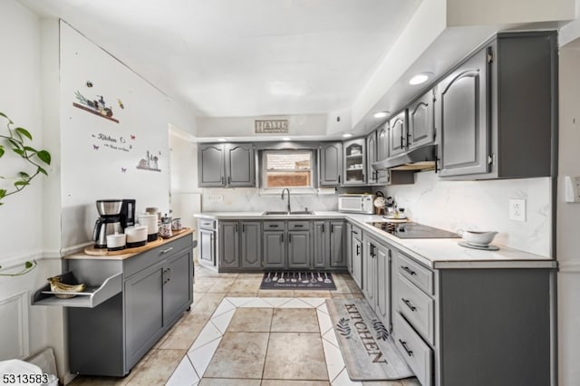 kitchen with gray cabinets, black electric stovetop, sink, backsplash, and light tile patterned floors