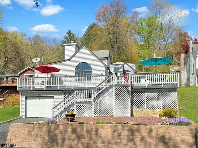 rear view of property featuring a garage, a wooden deck, and a lawn