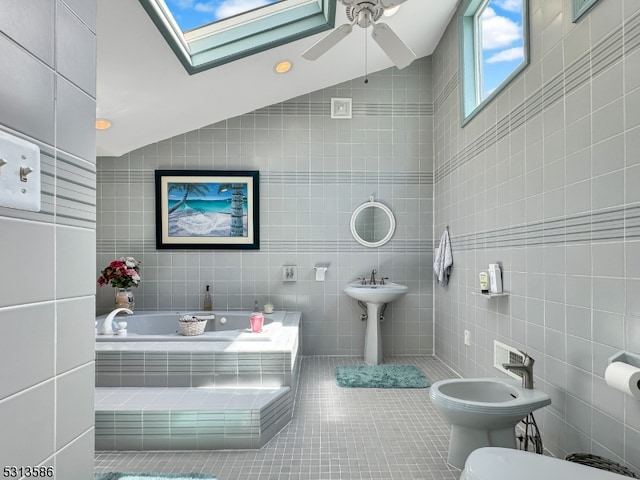 bathroom with vaulted ceiling with skylight, a bidet, a relaxing tiled tub, tile walls, and toilet