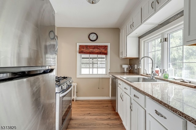 kitchen with appliances with stainless steel finishes, light hardwood / wood-style floors, white cabinetry, light stone countertops, and sink