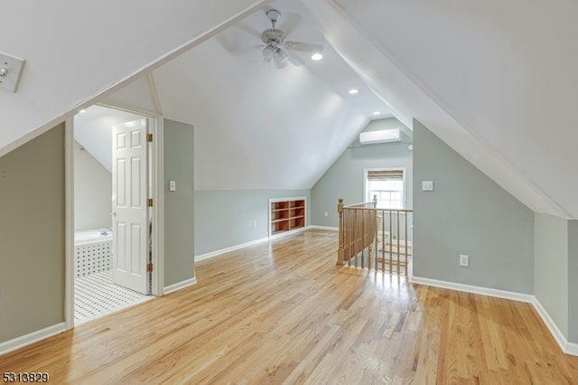 additional living space featuring ceiling fan, light wood-type flooring, vaulted ceiling, and a wall unit AC