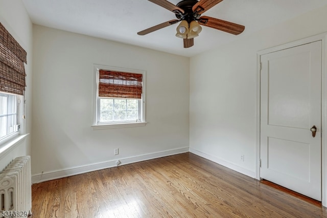 empty room featuring radiator, ceiling fan, hardwood / wood-style flooring, and a healthy amount of sunlight