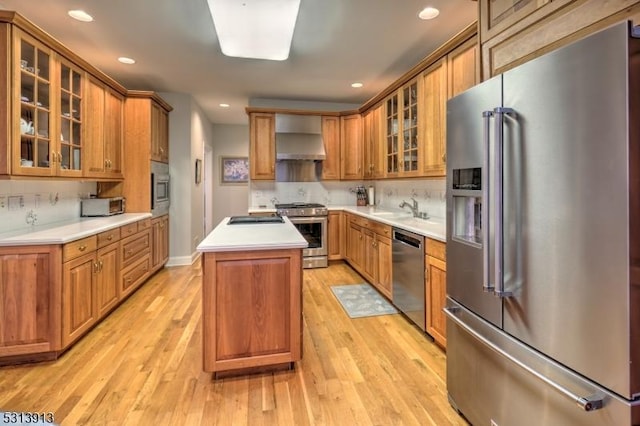 kitchen with a center island, sink, backsplash, appliances with stainless steel finishes, and wall chimney range hood