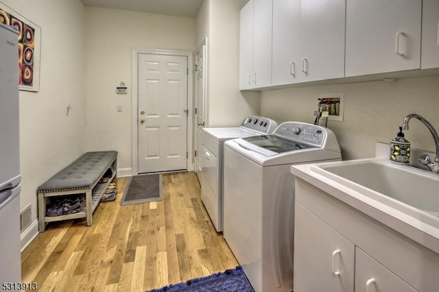 clothes washing area featuring sink, washing machine and dryer, light wood-type flooring, and cabinets